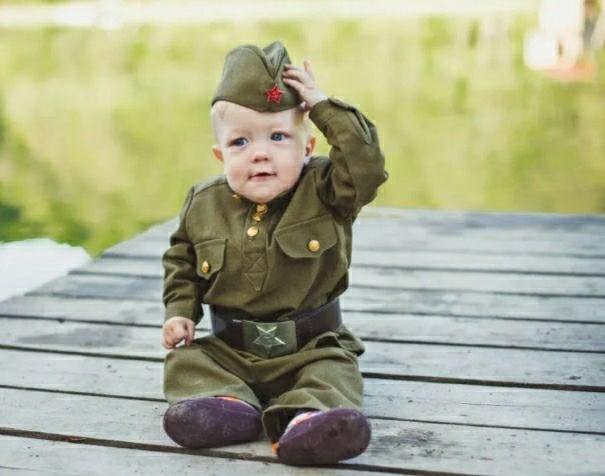 маленький мальчик в военной форме сидит на снегу